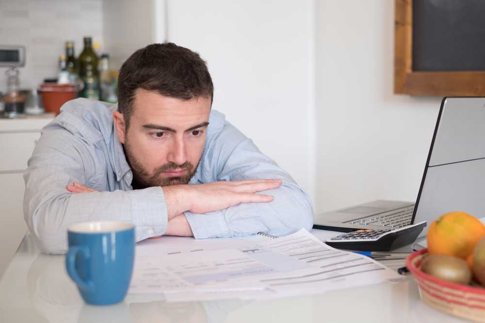 Sad man gone bankrupt sitting at desk by laptop