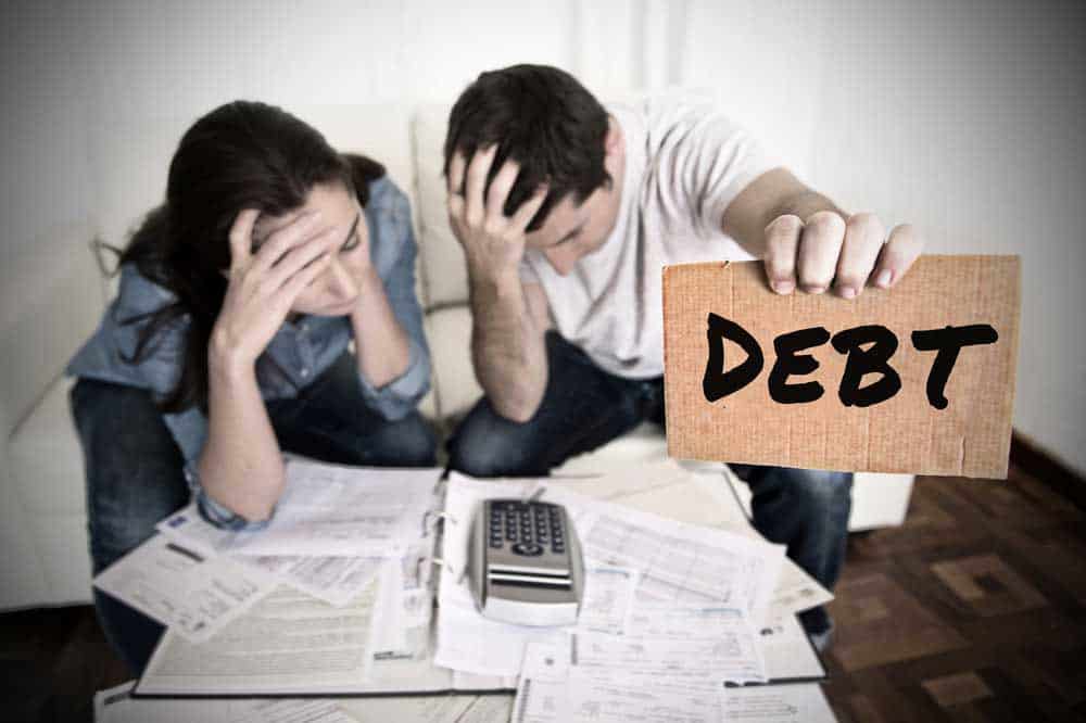 Couple worried about financial documents. Man holding a sign saying "Debt".