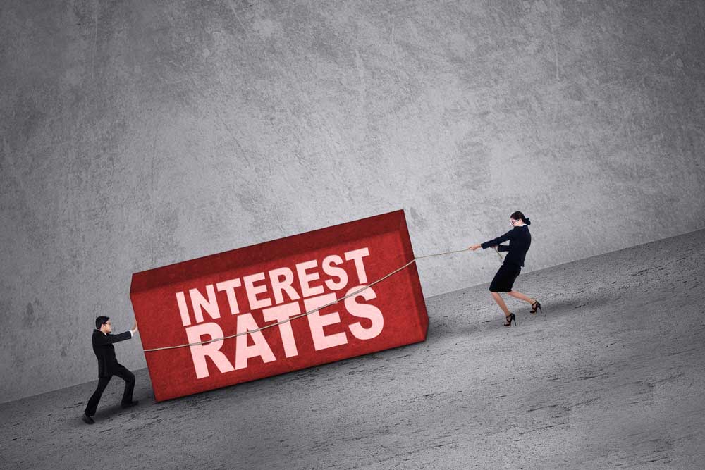 Man and woman dragging and pulling a big box with the words "Interest rates"