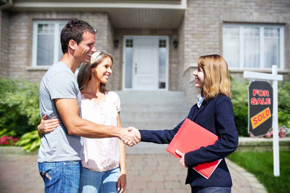 Young could shaking hands with real estate agent after buying a house. The new house in background.