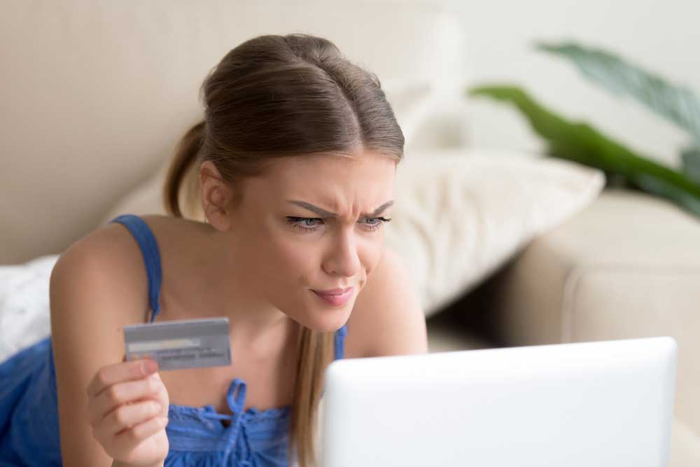 Credit card errors - Woman looking into her laptop holding a credit card in her right hand