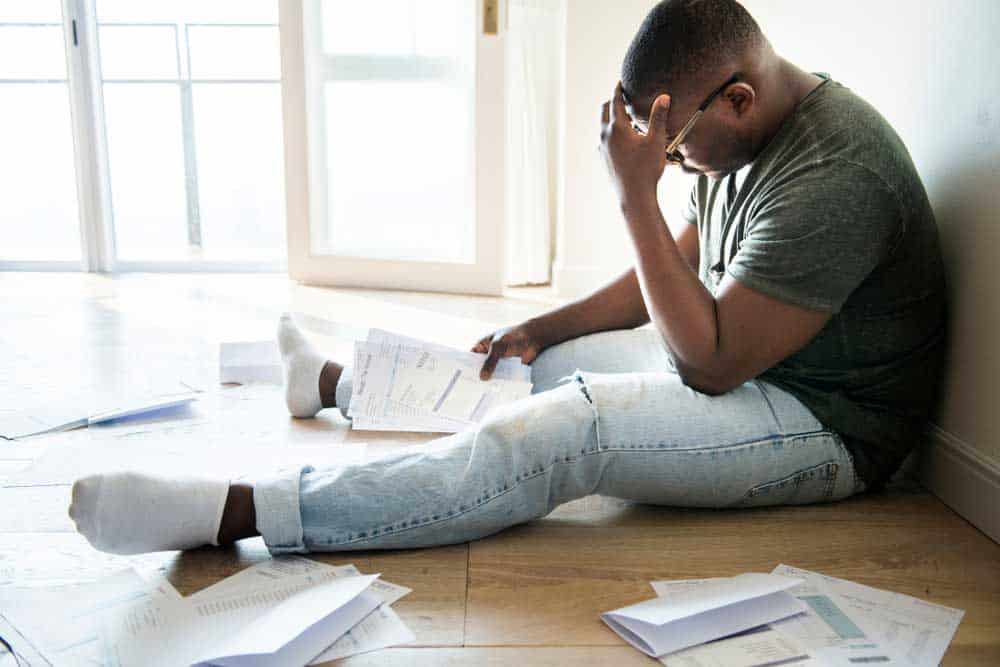 Frustrated man sitting on the floor with lots of bills