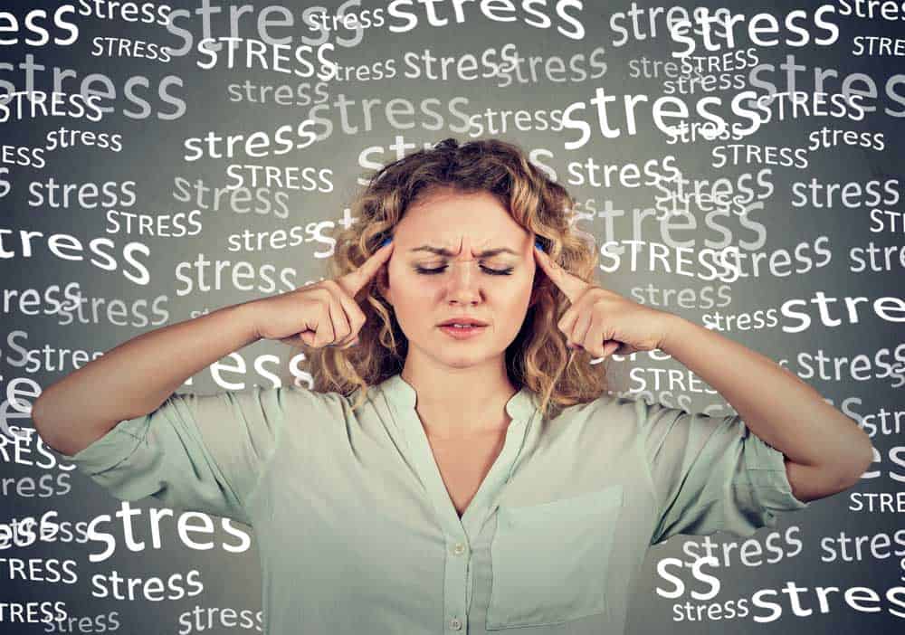 Woman holding fingers to her temples with the word "stress" written all over the background