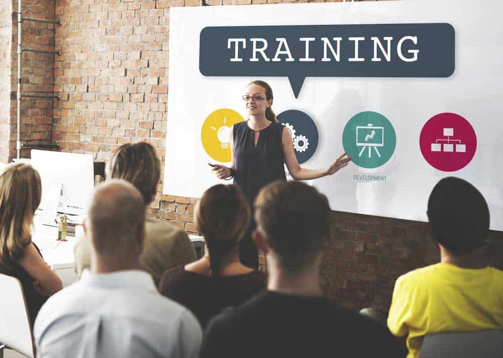 Teach training a group of employees in front of a whiteboard saying "Training"
