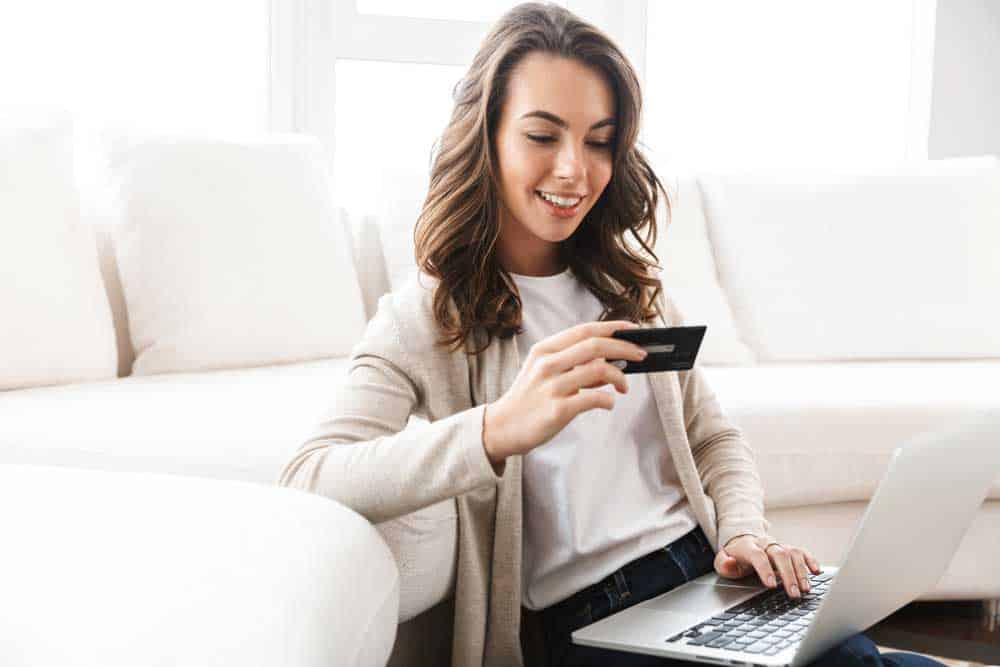 Woman sitting in couch with a credit card and her laptop