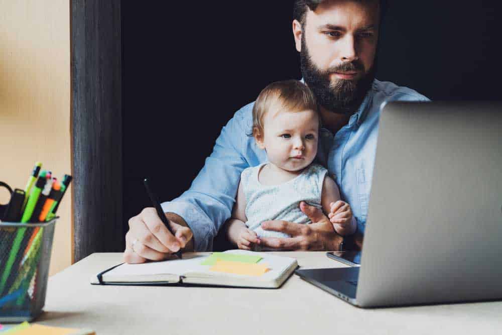 Bearded man working from home with a young child on his lap