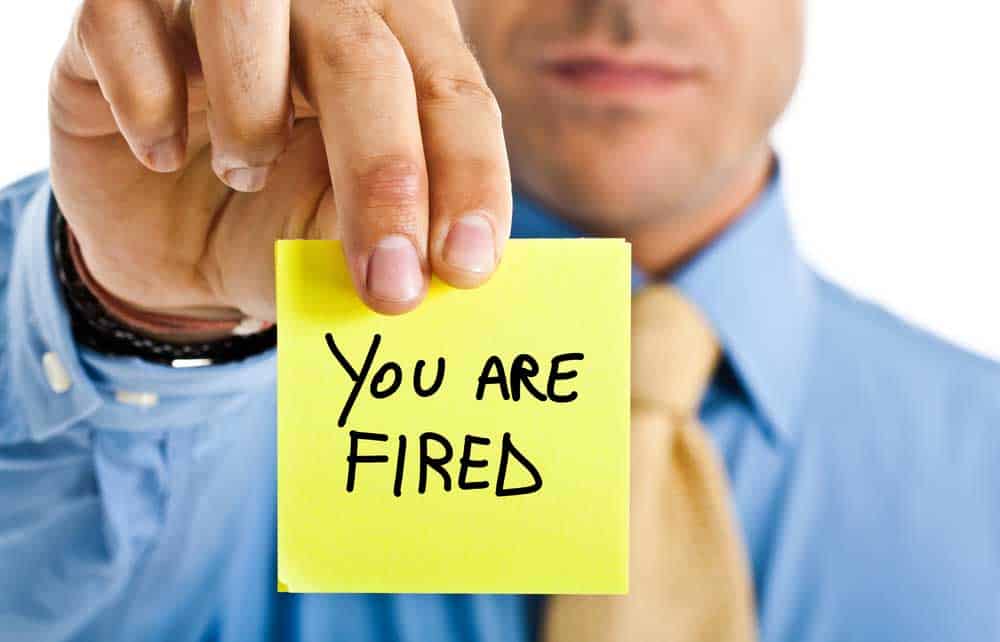 Man holding a post-it note with the words "You Are Fired"