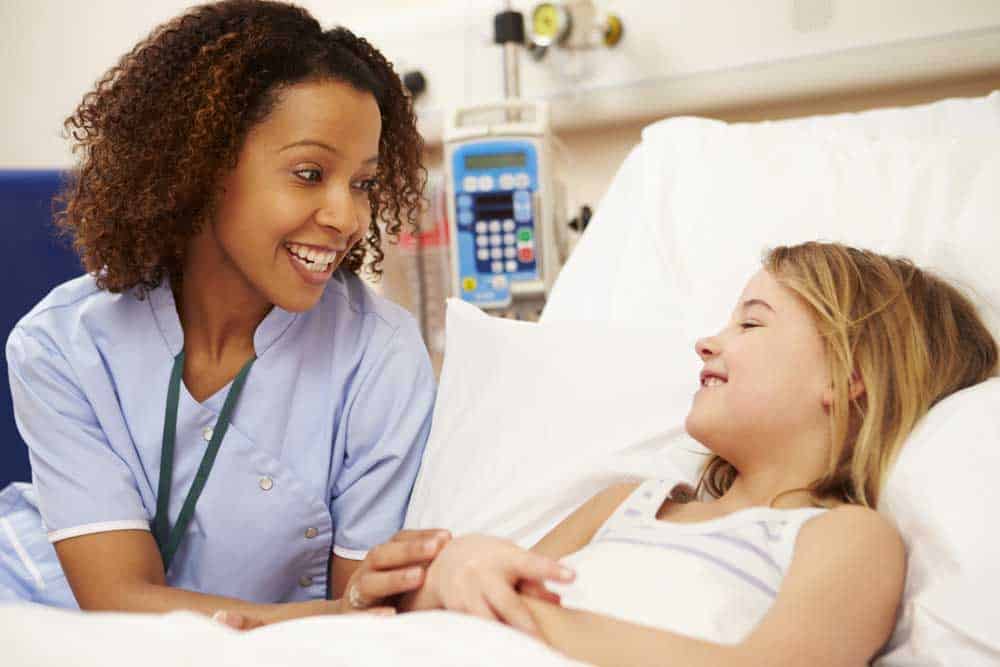 Young nurse talking to a female child in a hospital bed.