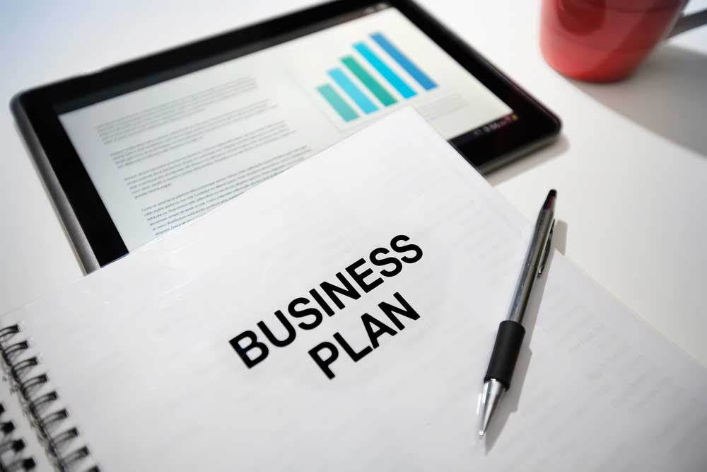 Close-up of a tablet, coffee mug, a pen and a piece of paper with the words "Business plan".