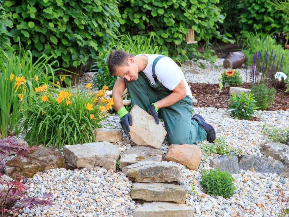 Gardner laying big natural rocks in a beautiful garden.