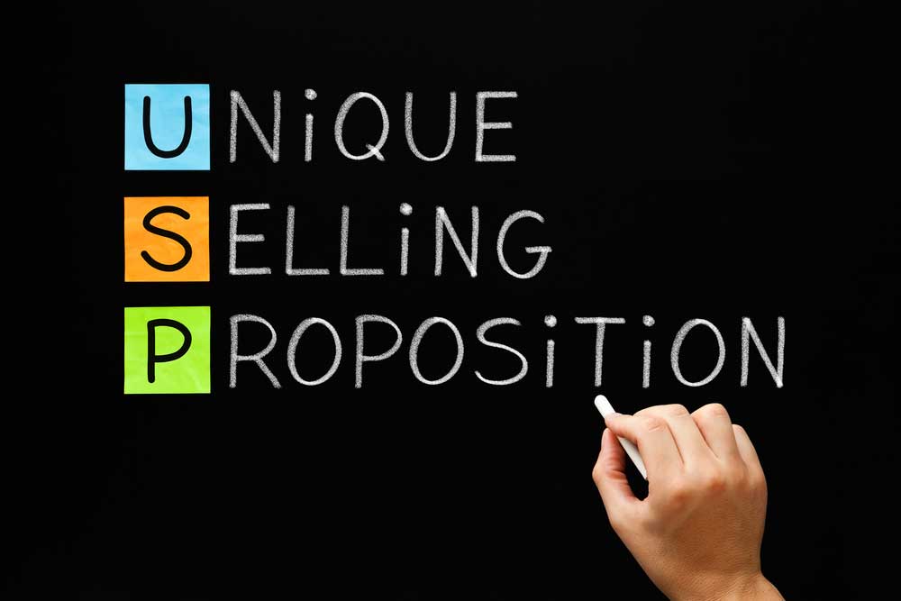 Hand writing the words "Unique Selling Proposition" on a blackboard.